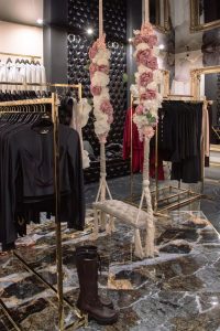 Wnętrze butiku LoveYa z eleganckim wystrojem – marmurowa podłoga, złote lustra, huśtawka ozdobiona kwiatami, oraz ubrania na wieszakach