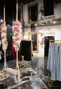 Wnętrze butiku LoveYa z eleganckim wystrojem – marmurowa podłoga, złote lustra, huśtawka ozdobiona kwiatami, oraz ubrania na wieszakach