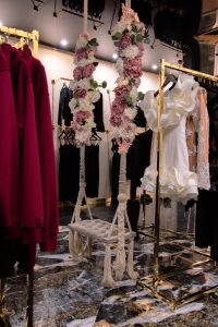 Wnętrze butiku LoveYa z eleganckim wystrojem – marmurowa podłoga, złote lustra, huśtawka ozdobiona kwiatami, oraz ubrania na wieszakach